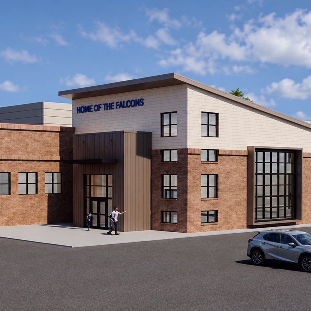 A modern brick and tan building with large windows and a sign reading "Home of the Falcons" above the entrance. Two people stand at the door, and a car is parked in the lot under a partly cloudy sky.